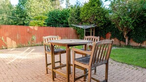 A patio with a round table and four wooden chairs, surrounded by a brick floor and a wooden fence. - Modern 4 Bedroom Detached House in Cardiff (Cardiff)