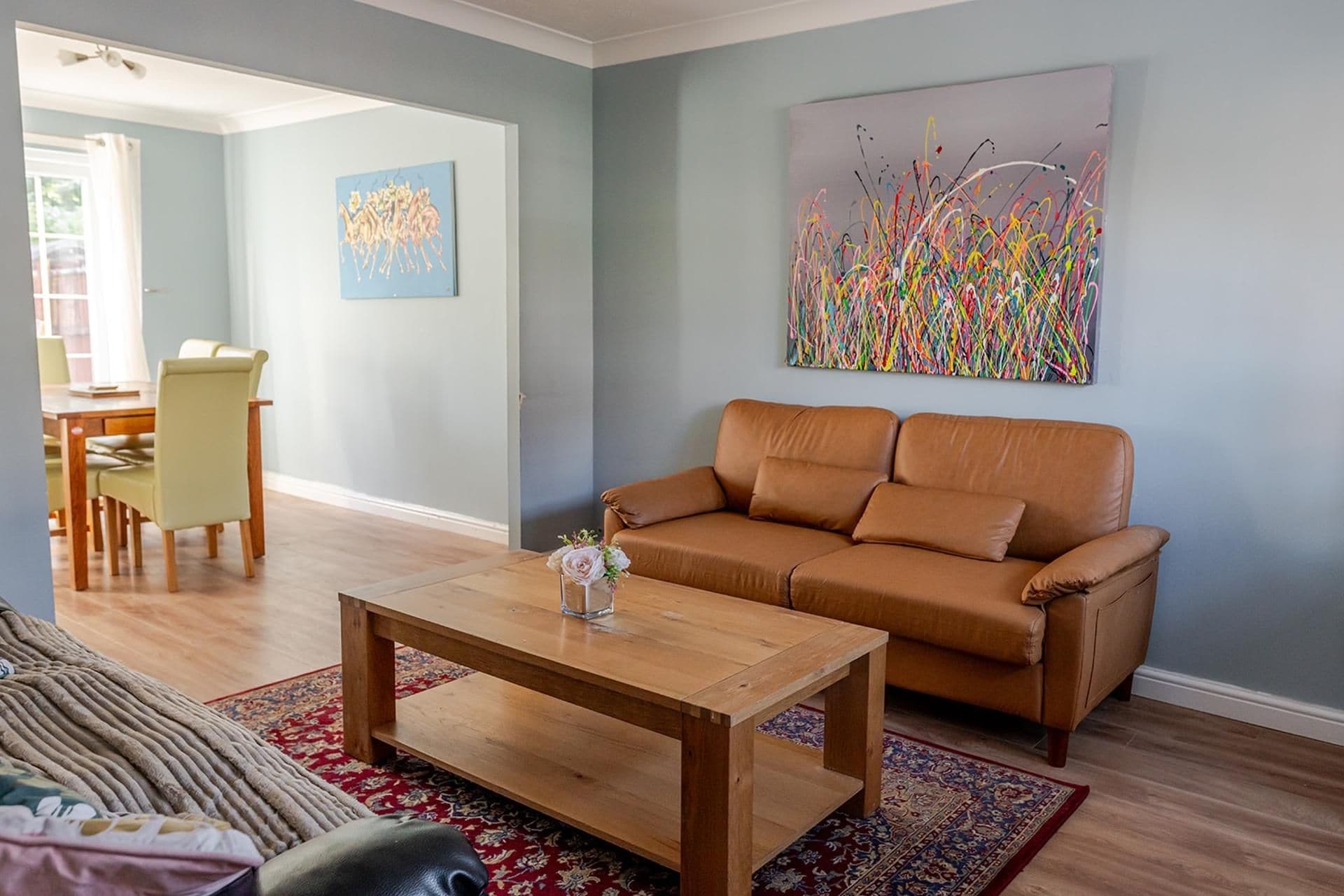 A living room with a brown leather sofa, a wooden coffee table, and a colorful abstract painting on the wall.