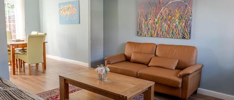 A living room with a brown leather sofa, a wooden coffee table, and a colorful abstract painting on the wall.