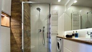 A modern bathroom with a glass-enclosed shower, a built-in washing machine, and a vanity with a mirror. - BP Apartment I (Torun)