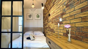 A modern bedroom with a brick wall, a wooden bedside table, a bed with white linens, and a hanging light fixture. - BP Apartment I (Torun)