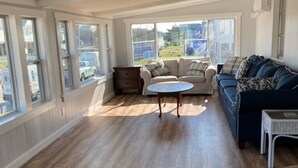Amplia sala de estar con piso de madera, una mesa redonda para café, dos sofás y ventanas grandes que ofrecen vistas al exterior.