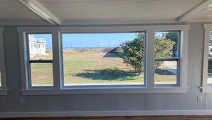 Una habitación con ventanas amplias, piso de madera y vistas a un campo cubierto de césped y edificios a lo lejos.