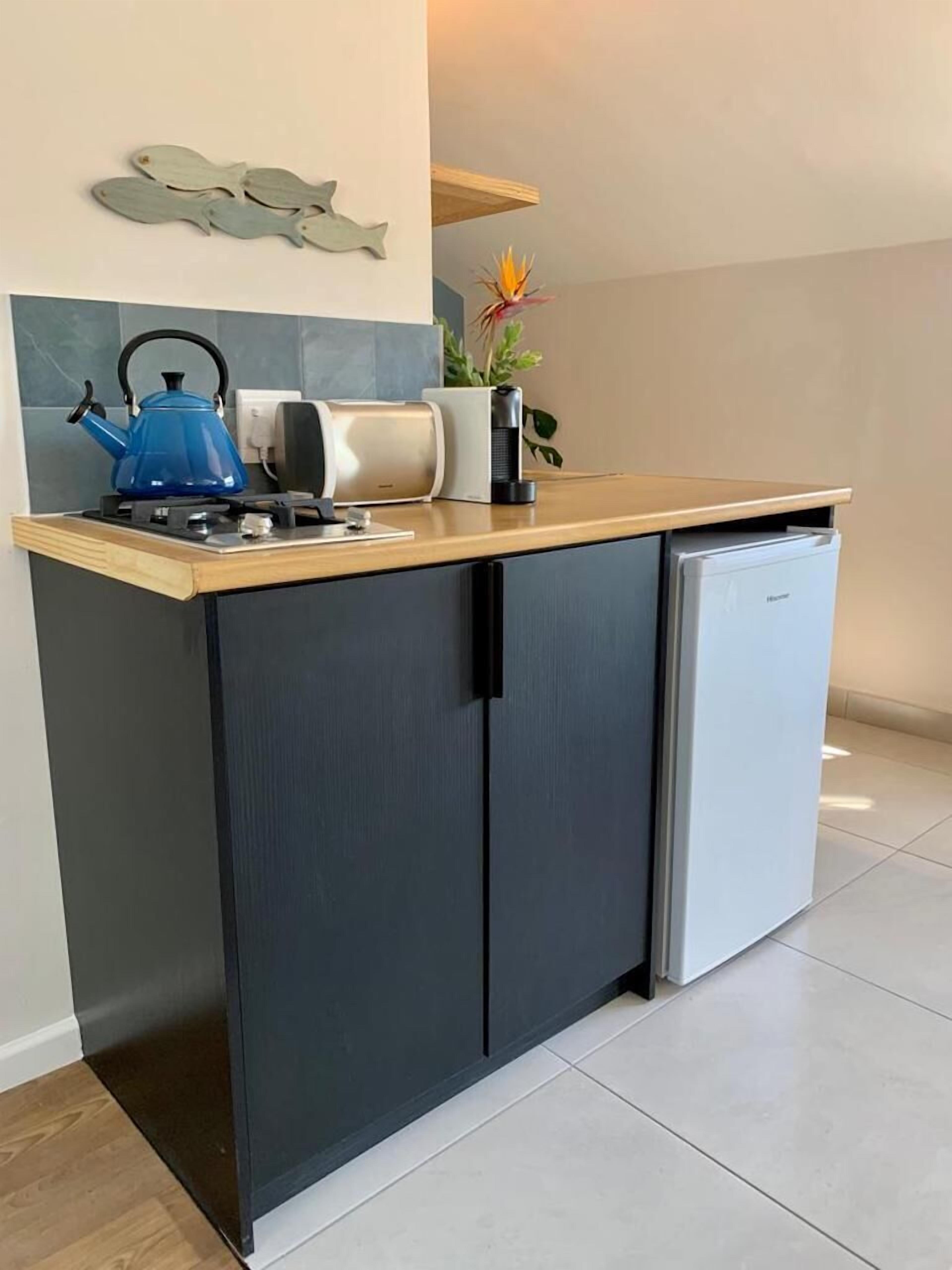 A compact kitchen with a built-in refrigerator, a kettle, a coffee maker, and a decorative fish wall art piece.