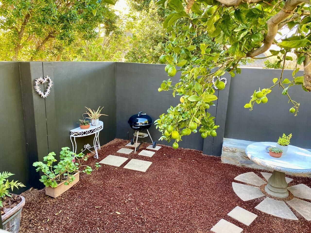 A patio area with a barbecue grill, a table with potted plants, and a decorative heart on the wall.