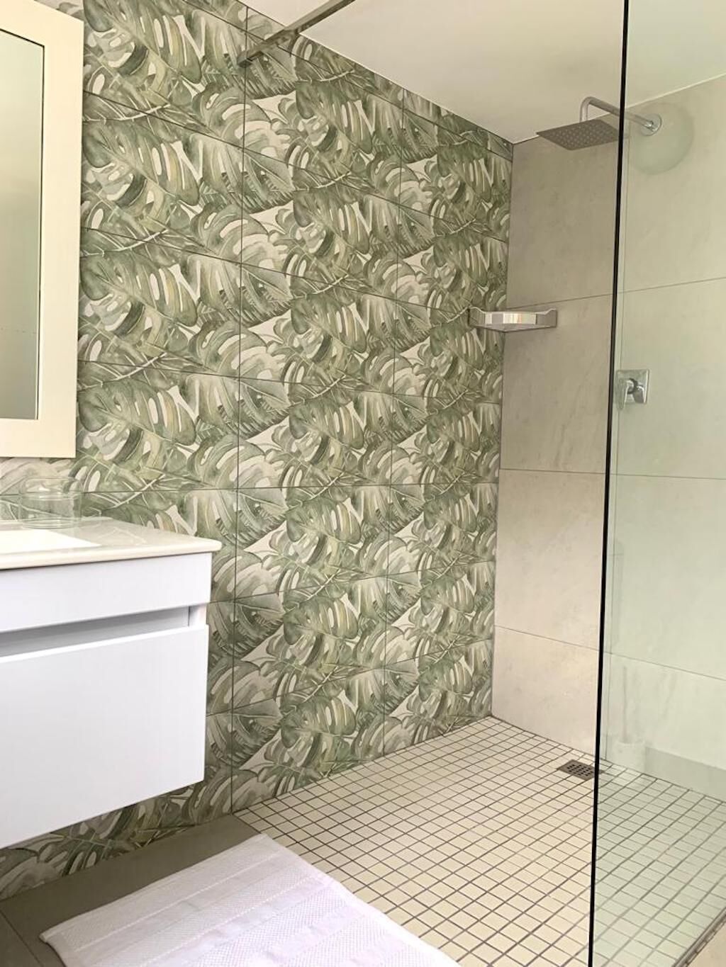 Un baño con pared estampada, cabina de ducha de vidrio y lavamanos blanco.