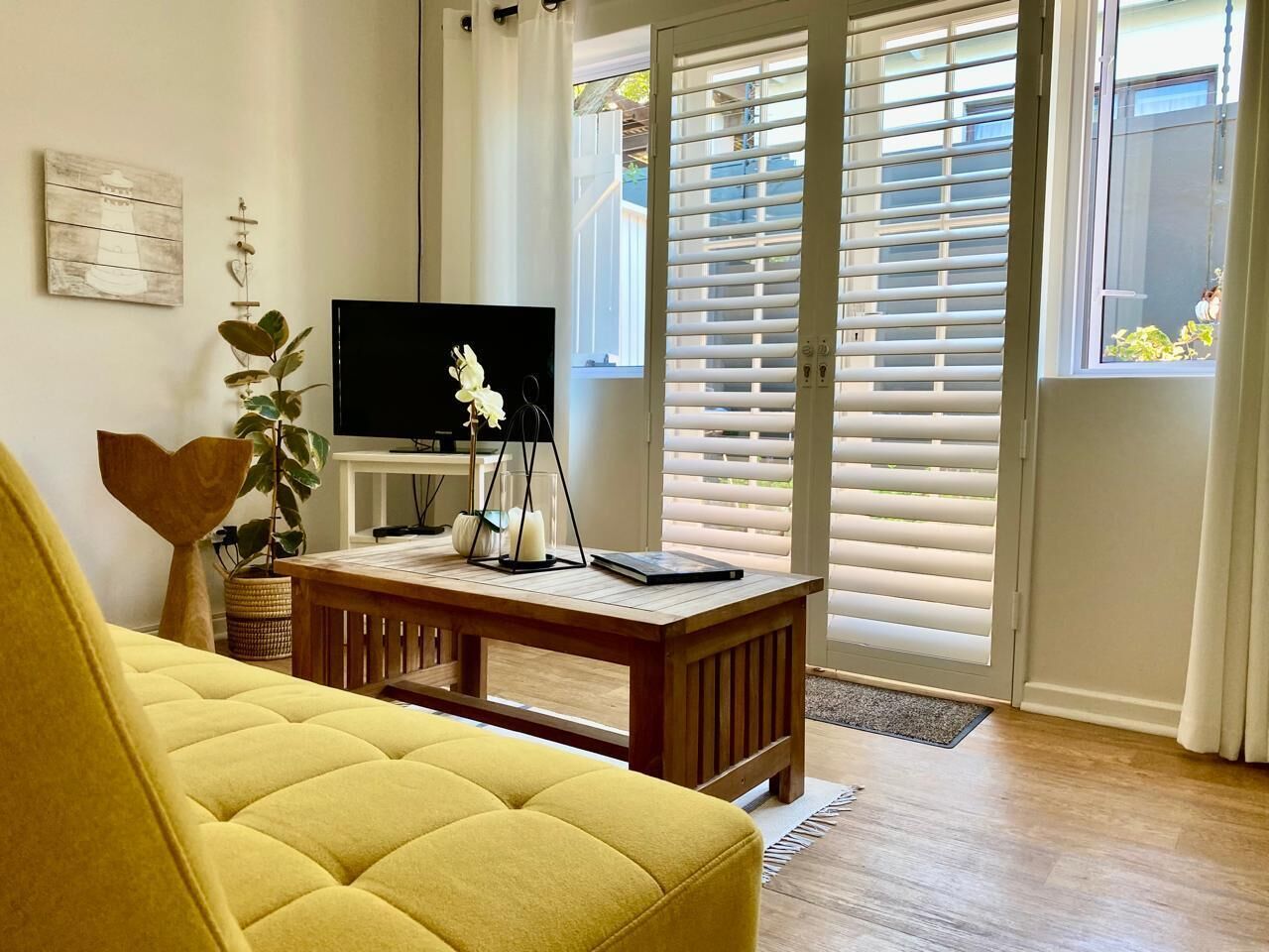 A living room with a yellow sofa, a wooden coffee table, a TV, and a sliding glass door with blinds.