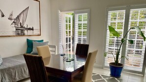 A dining area with a glass table, striped chairs, a blue potted plant, and a sailboat painting on the wall. - Anchor's Rest Hermanus (Hermanus)