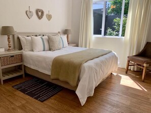 A bedroom with a bed, bedside tables, a chair, a window with curtains, and a view of the outside.