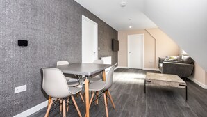 A modern dining area with a gray table and chairs, a wooden coffee table, and a gray textured wall. - Magna House (Egham)