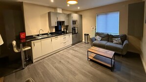A modern kitchen with grey cabinets, a black countertop, and a hanging light fixture. - Magna House (Egham)