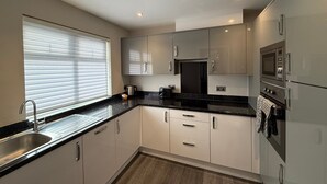 A modern kitchen with a sink, stove, microwave, and cabinets. - Magna House (Egham)