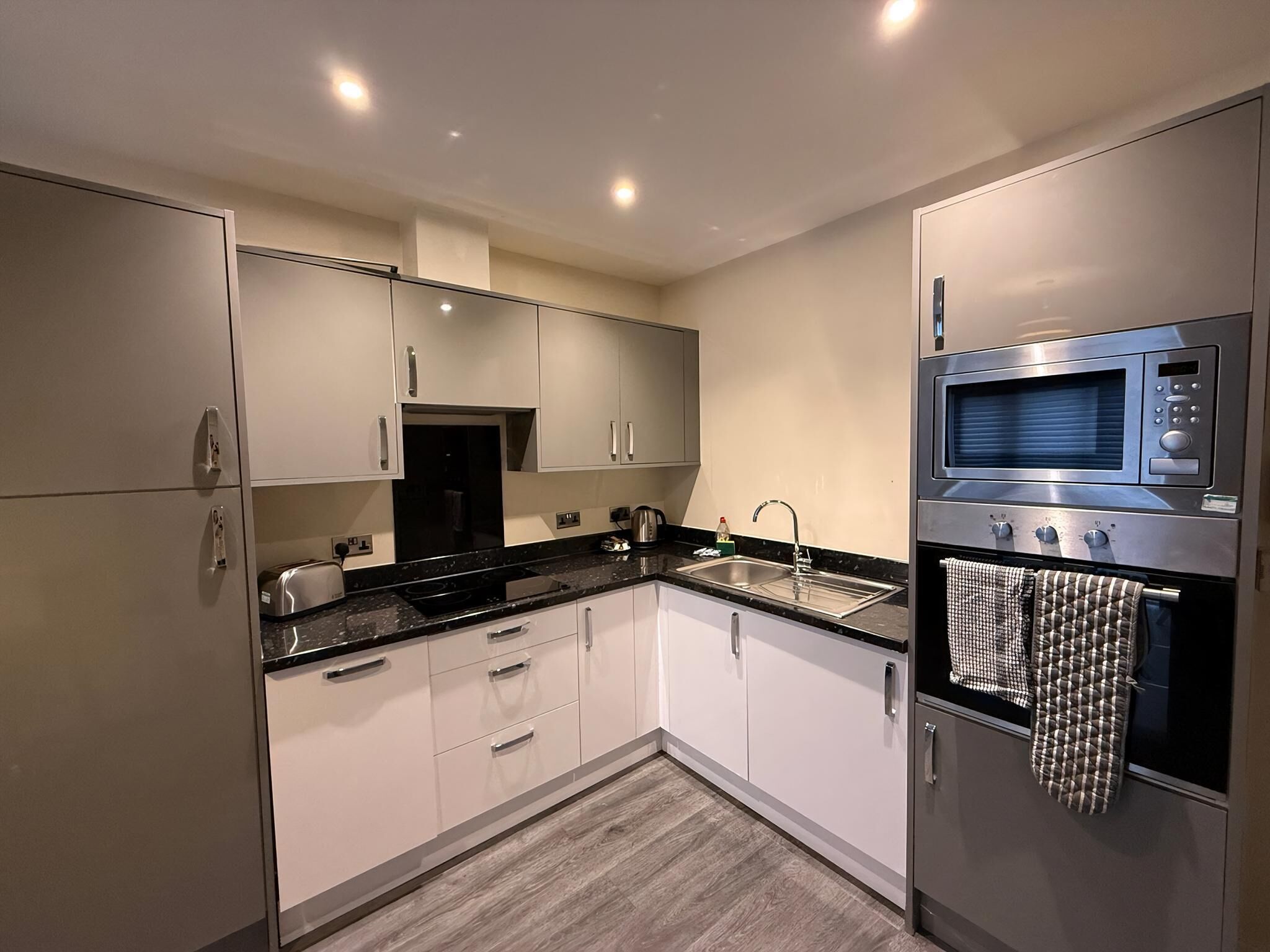 A modern kitchen with white cabinets, a black countertop, stainless steel appliances, and a wooden floor.