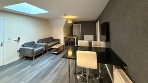 A modern apartment with a skylight, a sofa, a dining table, and a bar area. - Magna House (Egham)