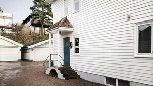 A white house with a blue door, a small porch, and a gravel driveway. - StayPlus Central Five Bedroom Home (Kristiansand)