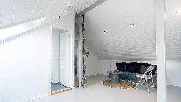 A spacious attic room with a high ceiling, a large window, a cozy seating area with a sofa and chairs, and a small round table. - StayPlus Central Five Bedroom Home (Kristiansand)