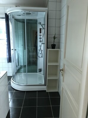 A modern bathroom with a glass-enclosed shower, white tiled walls, and a black tiled floor.