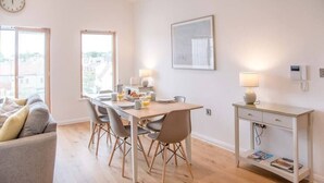 A modern dining area with a wooden table and chairs, a small side table with a lamp, and a framed picture on the wall. - 8 Deben Wharf, Woodbridge (Woodbridge)