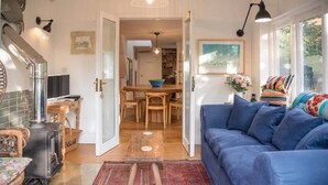 A cozy living room with a blue sofa, a fireplace, a dining area, and a large window. - The Coach House, Orford (Orford)