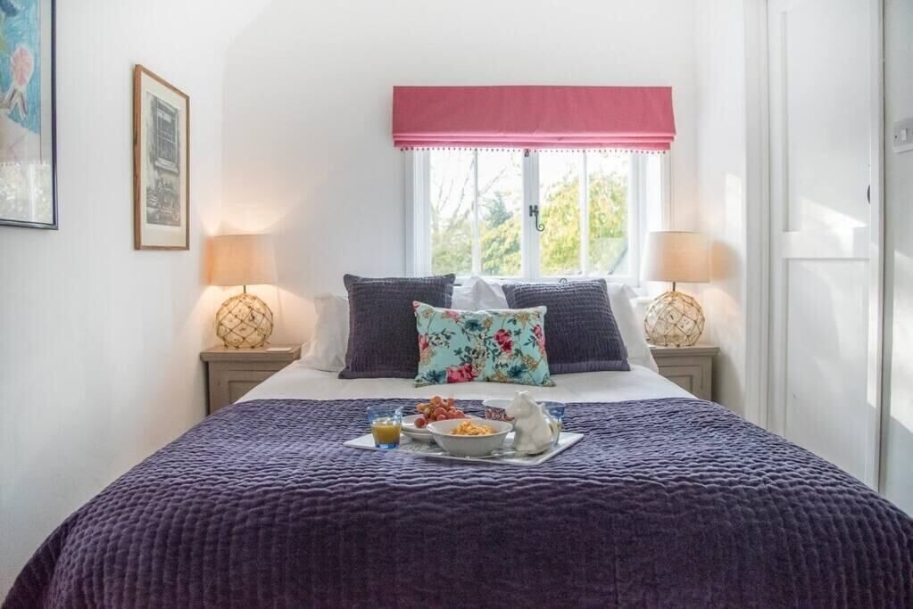 A neatly made bed with a purple blanket, a floral pillow, and a breakfast tray on the bed.
