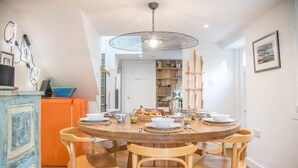 A dining area with a round wooden table set for four, surrounded by wooden chairs. There is a ceiling light fixture above the table. - The Coach House, Orford (Orford)