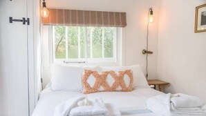 A hotel room with a bed, a window with a view of trees, a bedside lamp, and a door. - The Coach House, Orford (Orford)