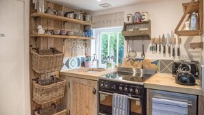 A kitchen with wooden shelves, hanging knives, and a kettle. - The Coach House, Orford (Orford)