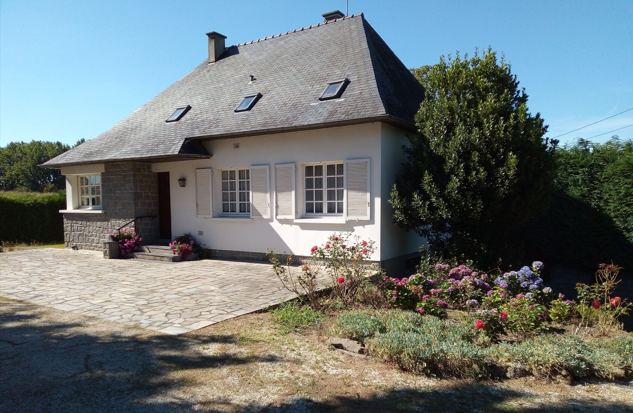 Een herenhuis met twee verdiepingen, een gevel van natuursteen, witte luiken en een pannendak.