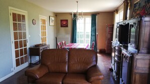 Una sala de estar con un sofá de cuero marrón, una mesa de centro de vidrio, un mueble de madera con un televisor y un comedor con mesa y sillas.