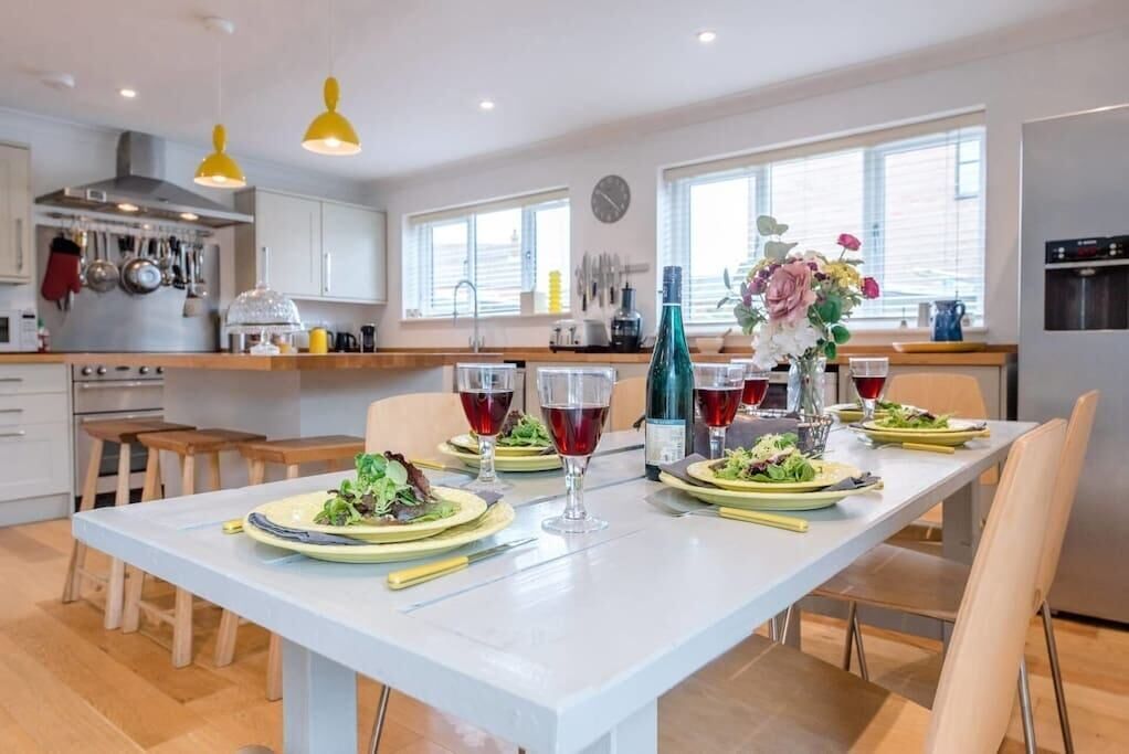 Une cuisine moderne avec des meubles blancs, une table à manger dressée pour quatre personnes, avec des assiettes, des verres et un vase de fleurs.