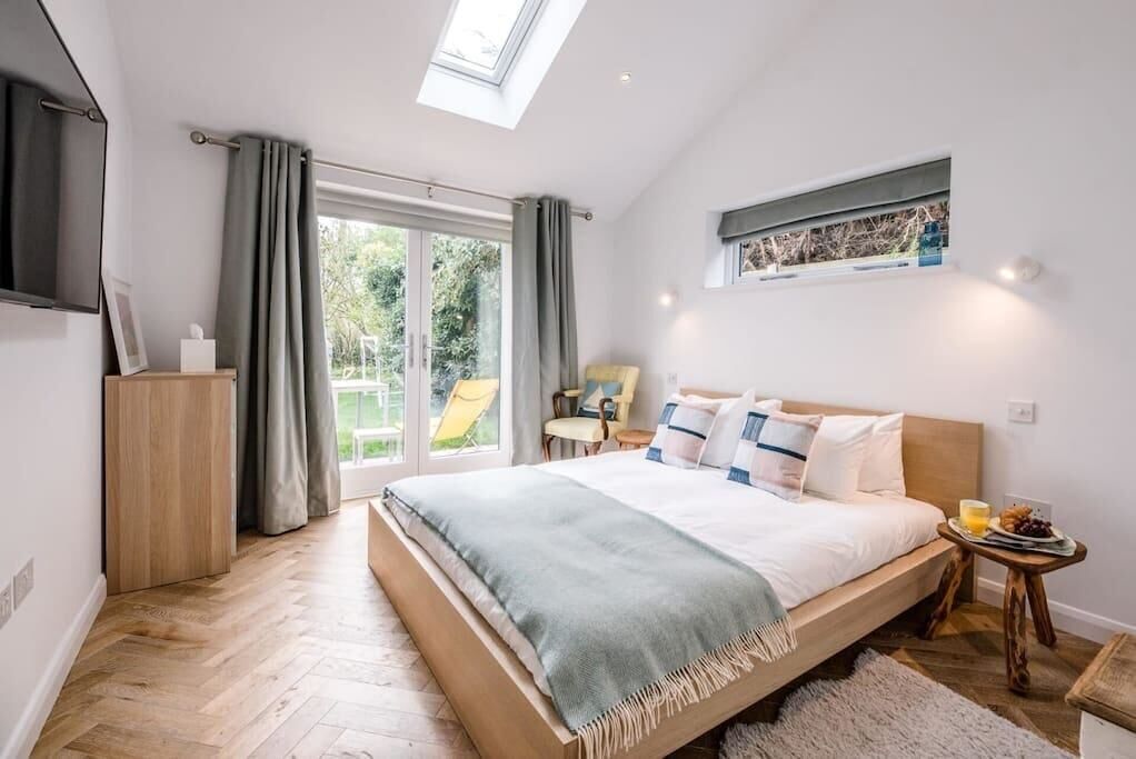 Une chambre avec un grand lit, une lucarne, une porte-fenêtre coulissante donnant sur un jardin et une petite table sur laquelle est disposée une assiette de fruits.