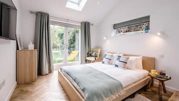 A bedroom with a large bed, a skylight, a sliding glass door to a garden, and a small table with a fruit plate.