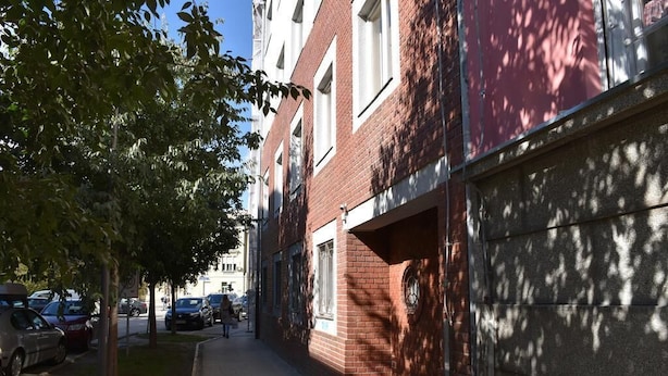 Una calle urbana estrecha con coches aparcados y acera.