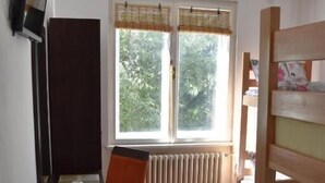 Una habitación con una cama litera, un escritorio con silla, un radiador y una ventana con persianas.