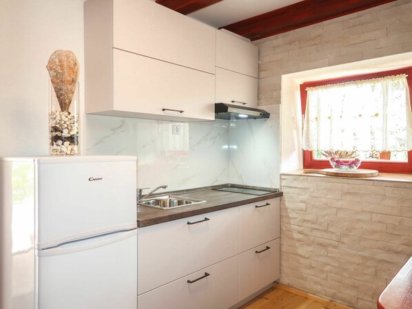 Una cocina con armarios blancos, un lavamanos empotrado y una ventana con cortinas florales.
