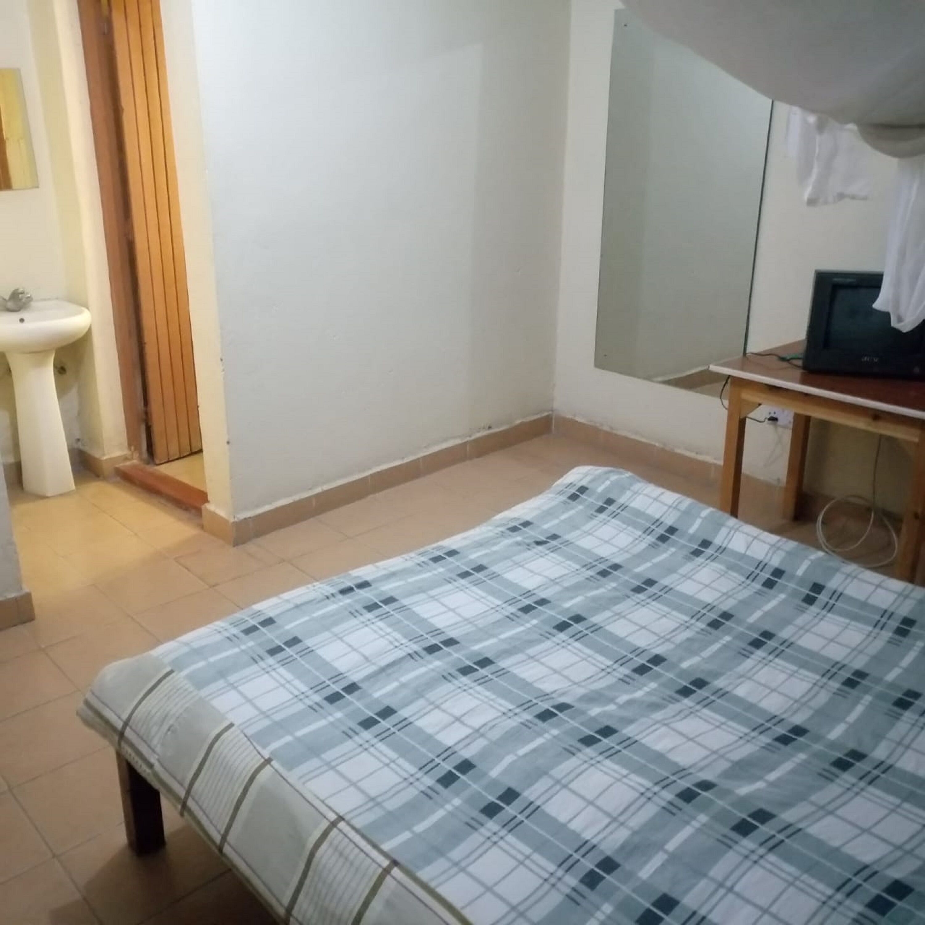 A bedroom with a bed, a small table with a television, a sink, and a mirror.