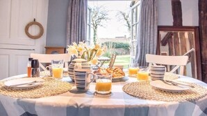 Une table de petit-déjeuner dressée avec des assiettes, des couverts, un pichet, des verres et un vase de fleurs.