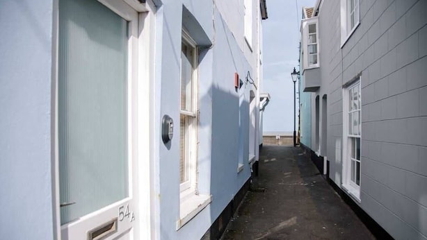A narrow alleyway between buildings with white walls and numbered doors, suggesting a residential or hotel setting.