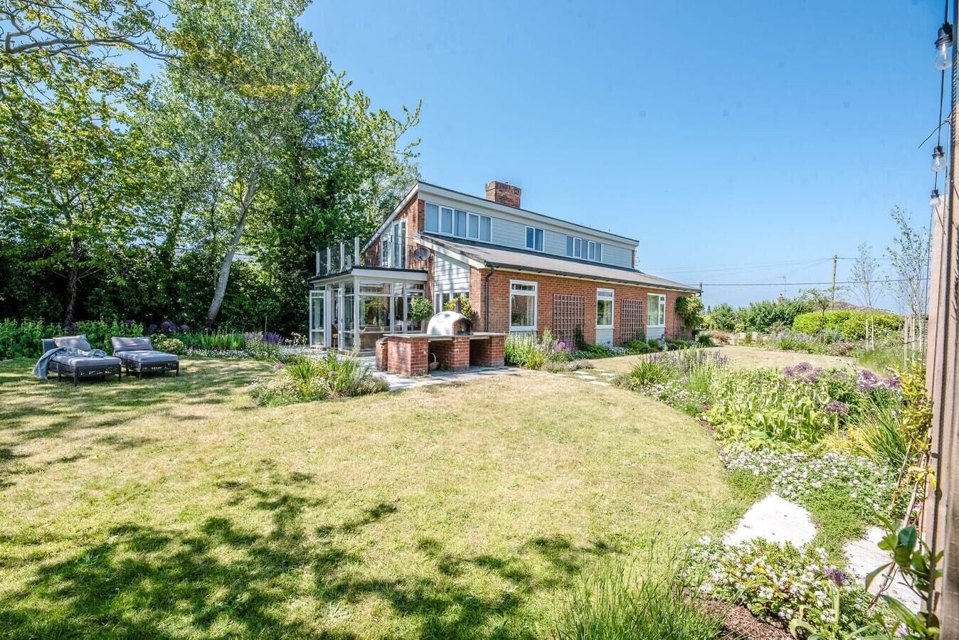 A two-story house with a brick exterior, a glass conservatory, and a barbecue area.