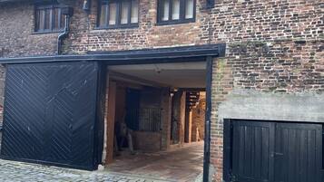 A traditional brick building with a large garage door, a cobblestone driveway, and a sloped roof with dormer windows.