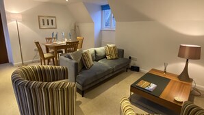 A modern living room with a sofa, striped armchairs, a coffee table, and a dining area with a table and chairs. - Bellfosters (King's Lynn)