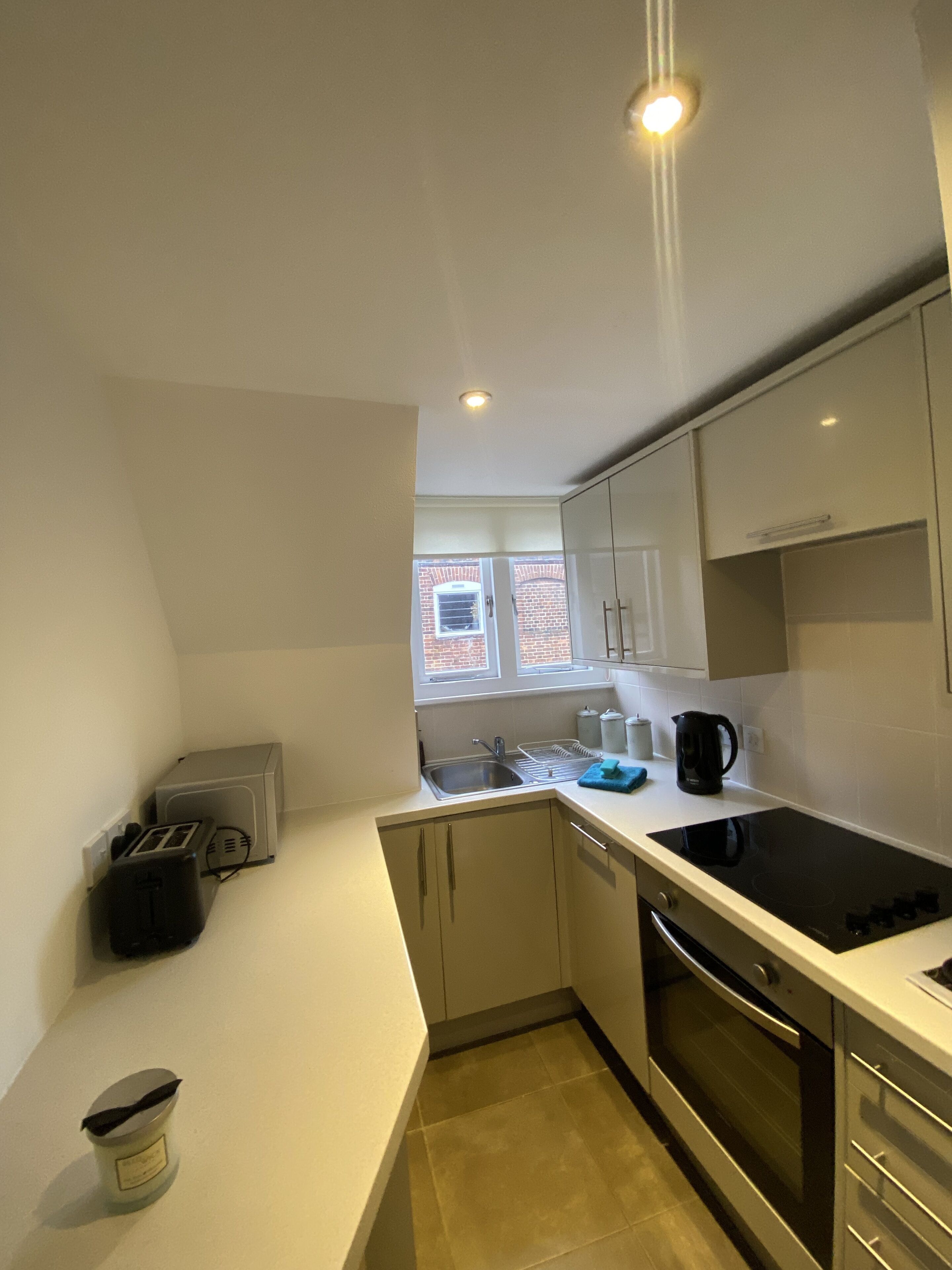 A compact kitchen with a built-in dishwasher, a stove, and a window with a view of a brick building.