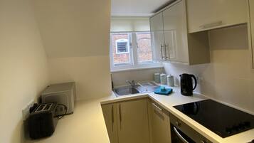A compact kitchen with a built-in dishwasher, a stove, and a window with a view of a brick building.