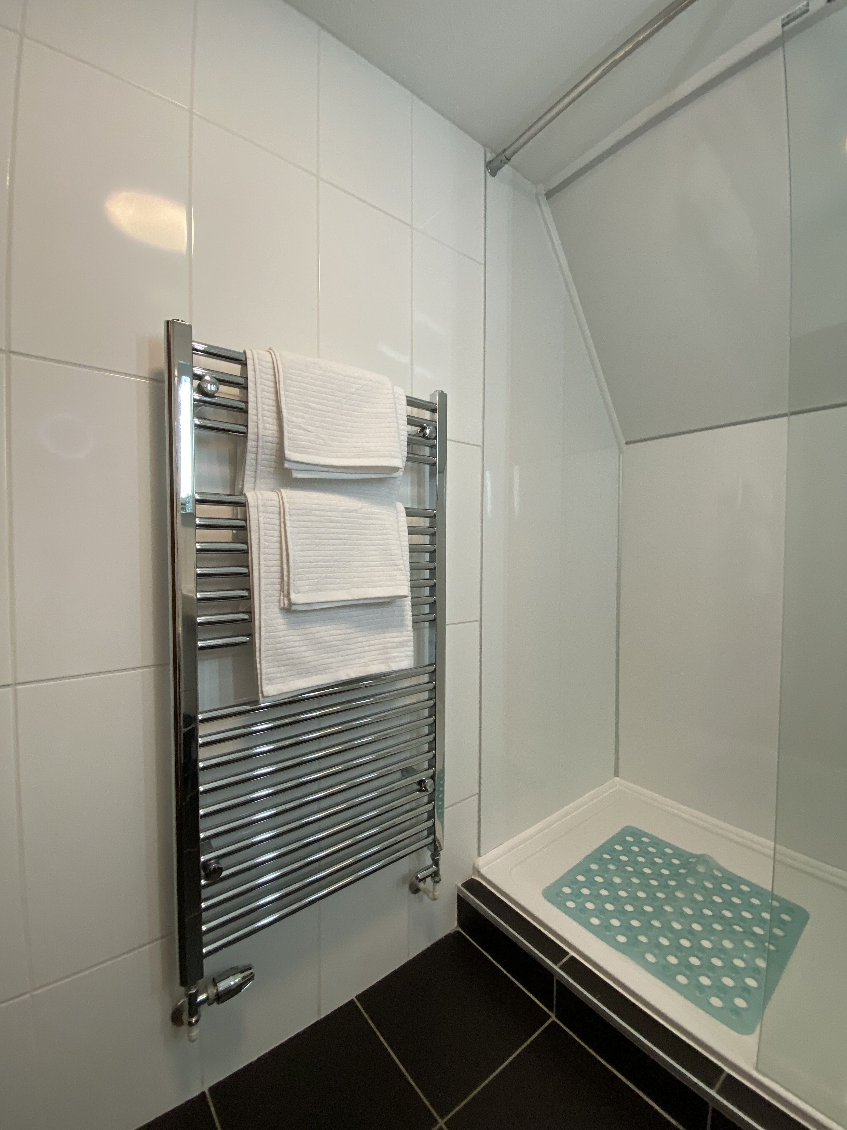 A shower area with a glass enclosure, a chrome towel rack with two towels, and a green non-slip mat on the floor.