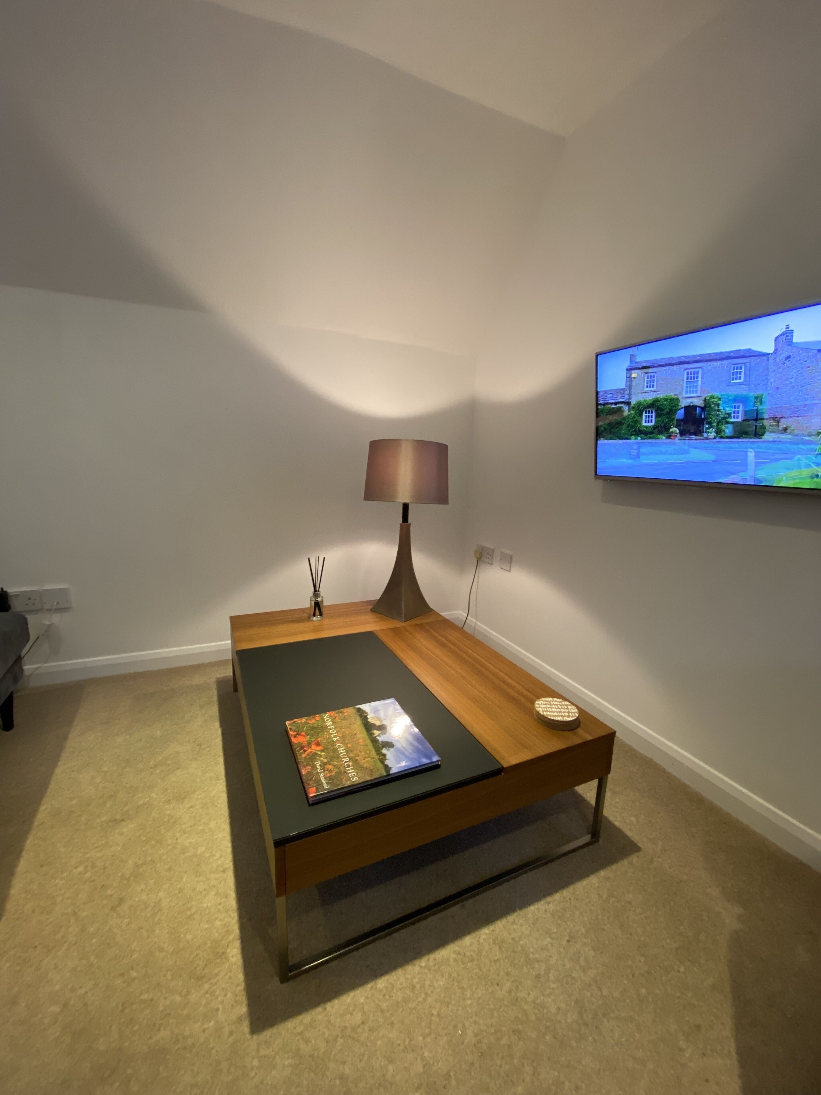 Una sala de estar moderna con una mesa de centro de madera, una lámpara, un libro y un televisor de pantalla plana montado en la pared.