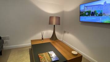 Una sala de estar moderna con una mesa de centro de madera, una lámpara, un libro y un televisor de pantalla plana montado en la pared.