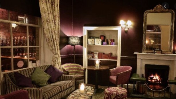 A cozy living room with a sofa, armchairs, a small table, and a bookshelf. A fireplace is visible in the background. - Bellfosters (King's Lynn)