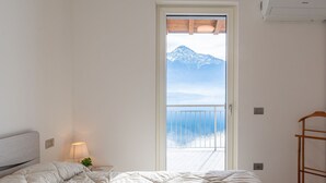 A bedroom with a bed, a nightstand, a lamp, a wooden chair, and a view of mountains through a door.