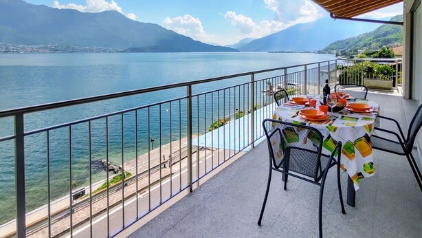 A balcony with a table set for dining, overlooking a lake with mountains in the background.