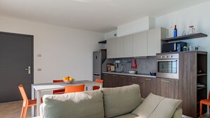A modern kitchen with built-in appliances, a dining area with a bowl of fruit, and a cozy seating area with a sofa.